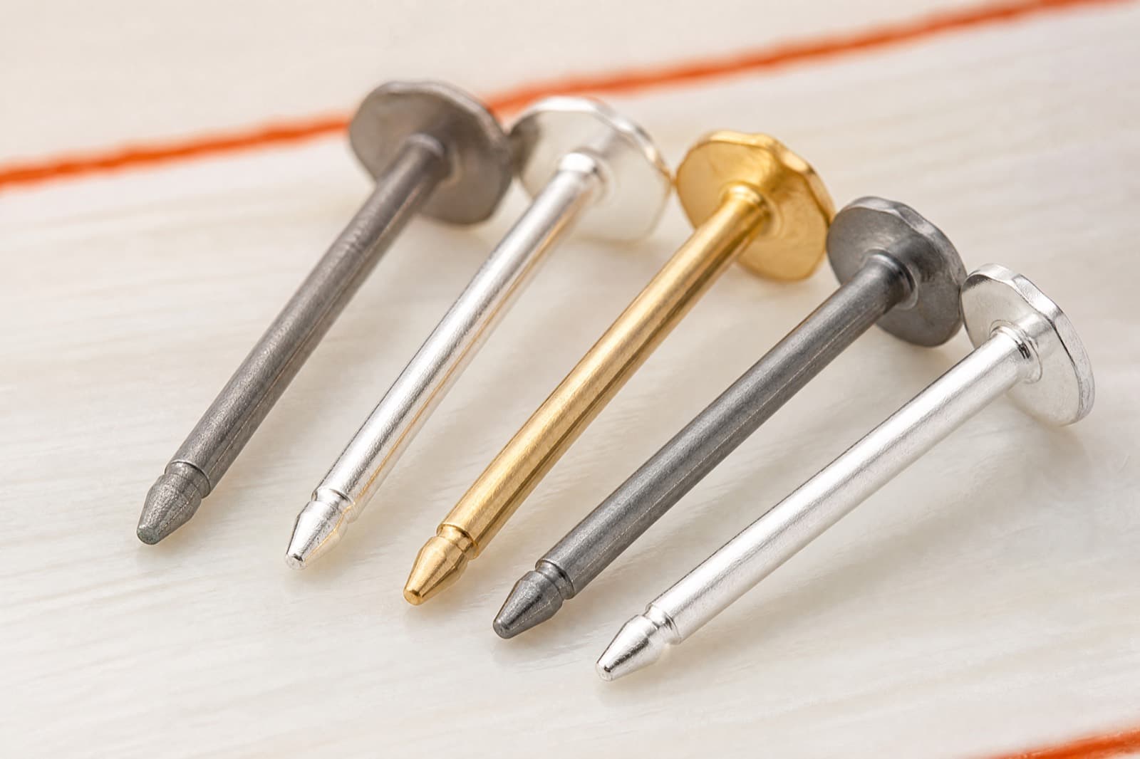 Five earring posts in titanium, silver and gold arranged in a fanned row, photographed at high magnification