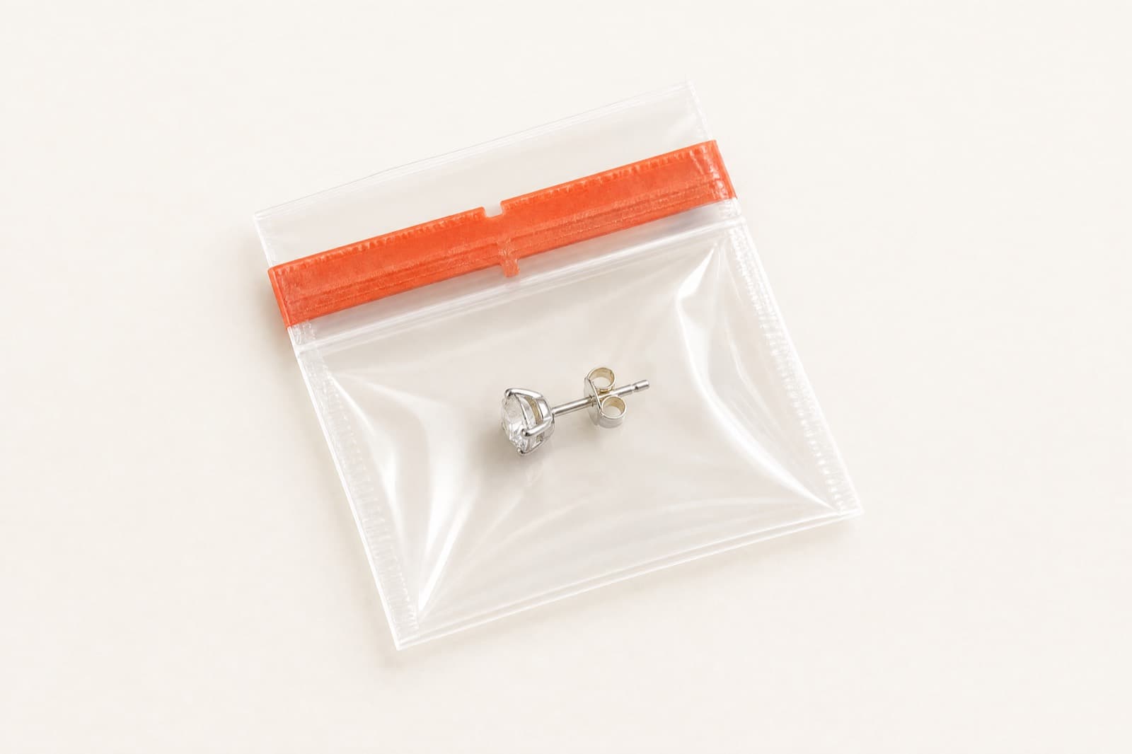 A single stud earring inside a sealed transparent pack closed with a tamper-evident seal strip
